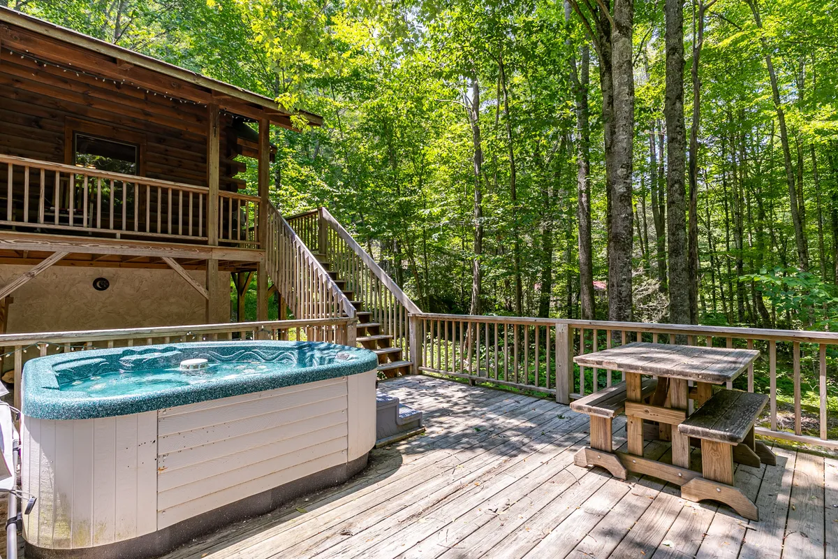 An inviting wooden deck extends out into the scenery, featuring a private hot tub and dining table surrounded by trees. The space offers opportunities for stargazing, outdoor dining, and quiet relaxation—a perfect spot for couples seeking seclusion and comfort in nature.
