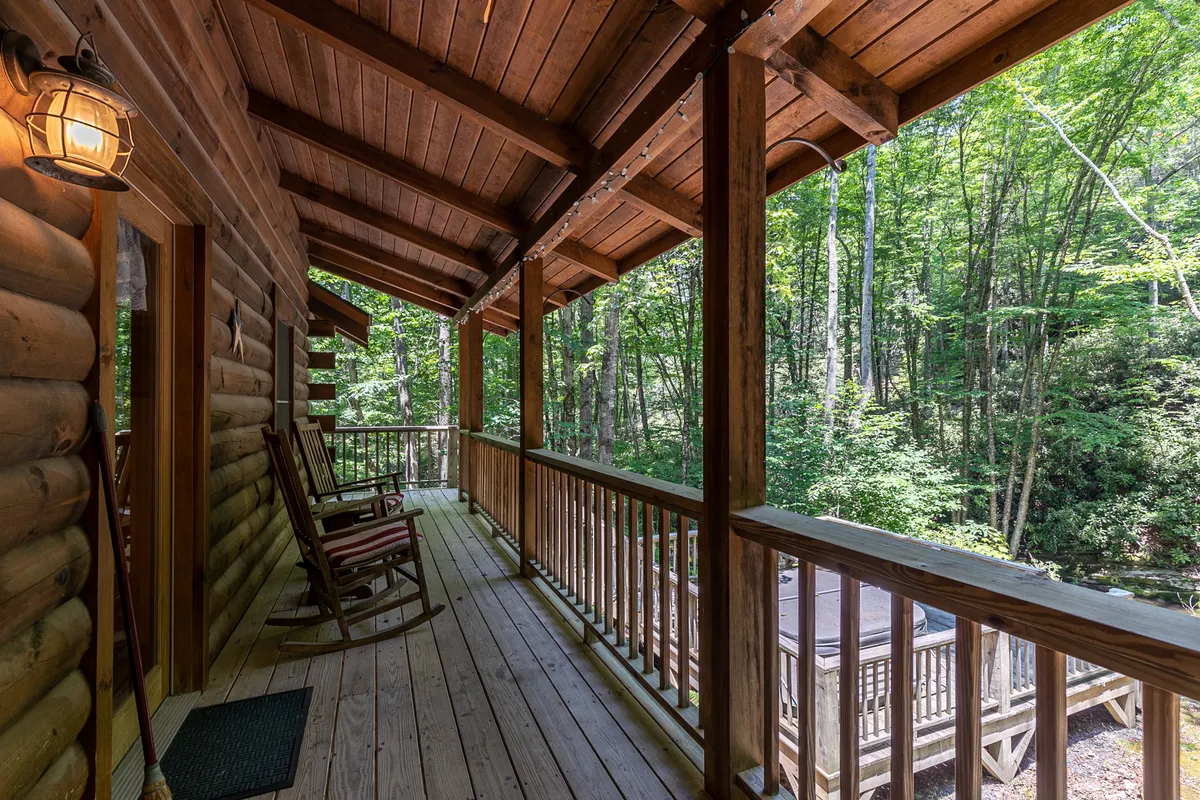 This image captures a classic wooden deck lined with comfortable rocking chairs, framed by lush greenery and the signature log cabin architecture. The mood is serene and welcoming, inviting guests to relax and take in the mountain air.