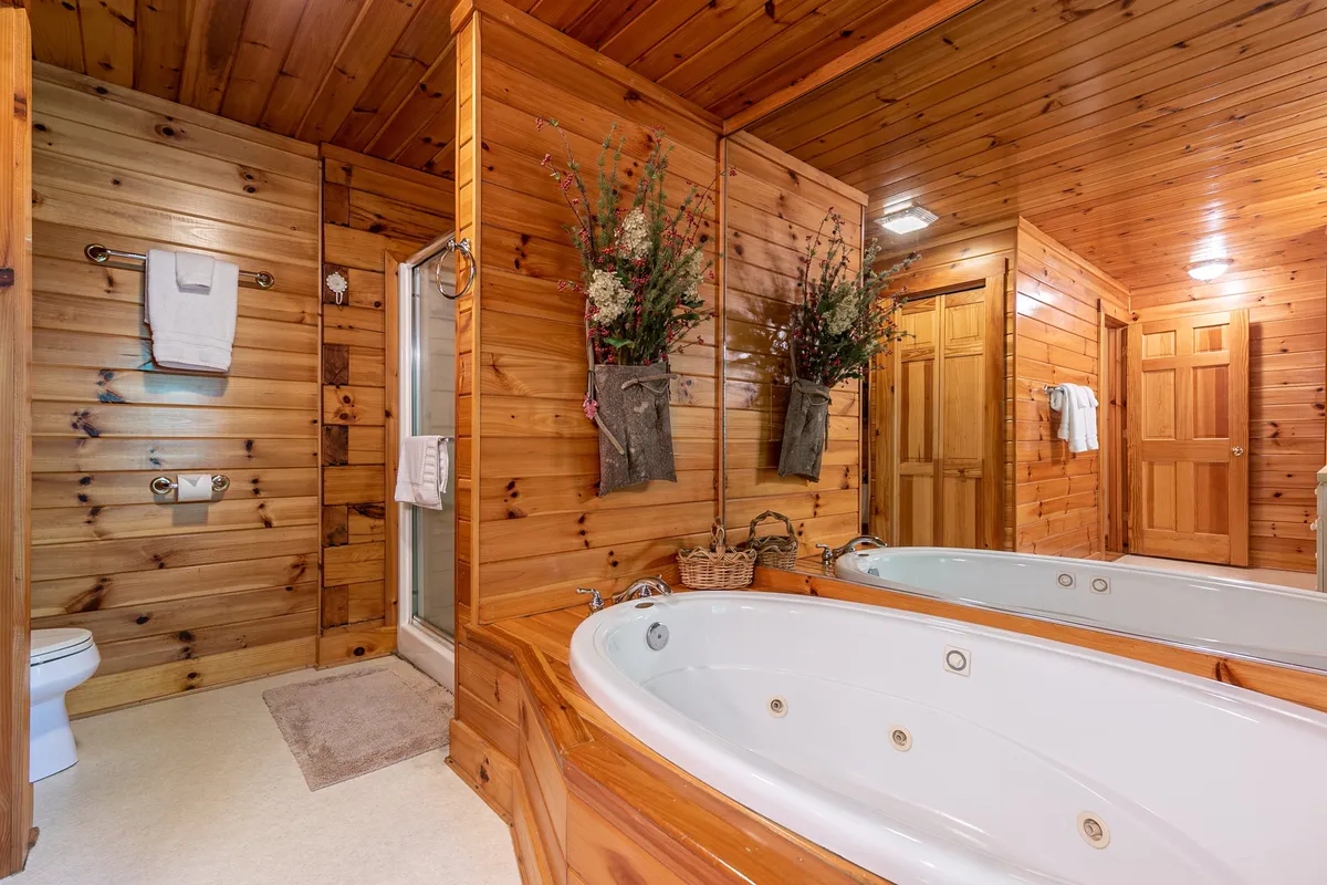 An inviting bathroom scene featuring whirlpool tubs set against wooden walls, decorative flowers adding a touch of romance, and a separate shower area within view. The space exudes a tranquil, spa-like ambiance ideal for relaxing soaks or rejuvenating showers.