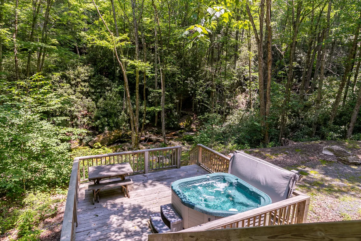 A private hot tub is nestled on a wooden deck, enveloped by verdant foliage. The scene exudes comfort and peace, offering glimpses of nature from the bubbling warmth of the tub.